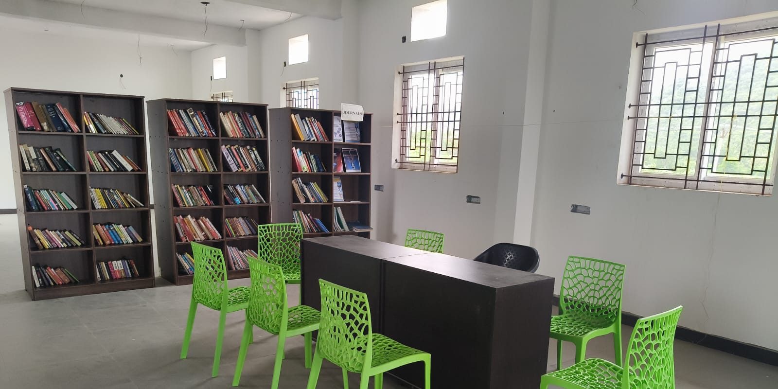College library with stocked bookshelves, a reading table and green chairs